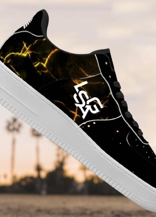 The LIONSGALA - LSGA Dorado Bolted Gold streetwear sneakers by LIONSGALA Brands feature a black design with bold yellow lightning streaks, white LSR lettering, and a thick white sole, set against palm trees in the background.