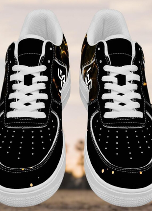 The LIONSGALA - LSGA Dorado Bolted Gold Streetwear Sneakers by LIONSGALA Brands feature black premium leather, white laces and soles, orange-yellow spot accents, and a stylized white logo, showcased outdoors against a blurred background.